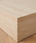 Close-up of the Sur Square Coffee Table’s corner on a wooden floor, showcasing the natural texture and linear patterns of its light beige travertine surface.