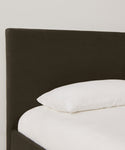 A neatly made Pacific Bed with a dark, upholstered headboard and a single white pillow in luxurious Belgian Libeco linen, set against a plain light-colored wall.